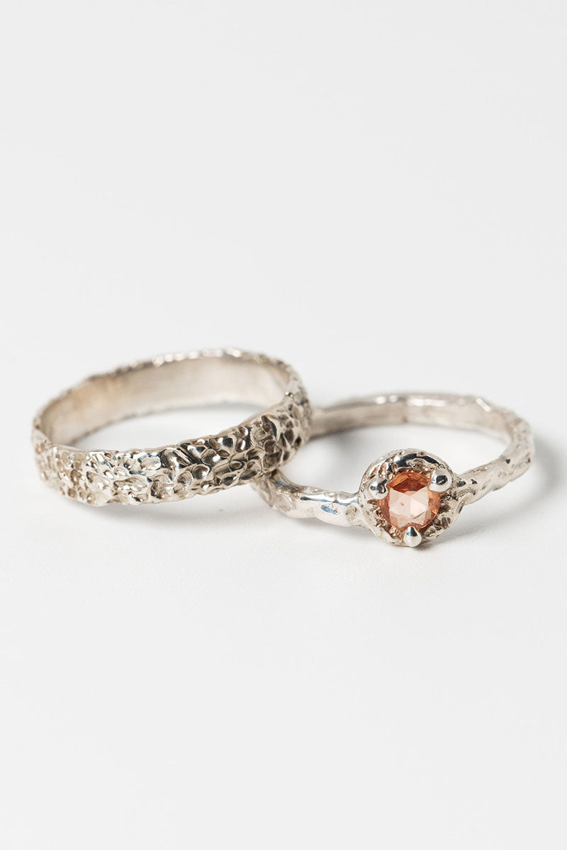 Pair of textured silver stacking rings with round peach sapphire cast in place