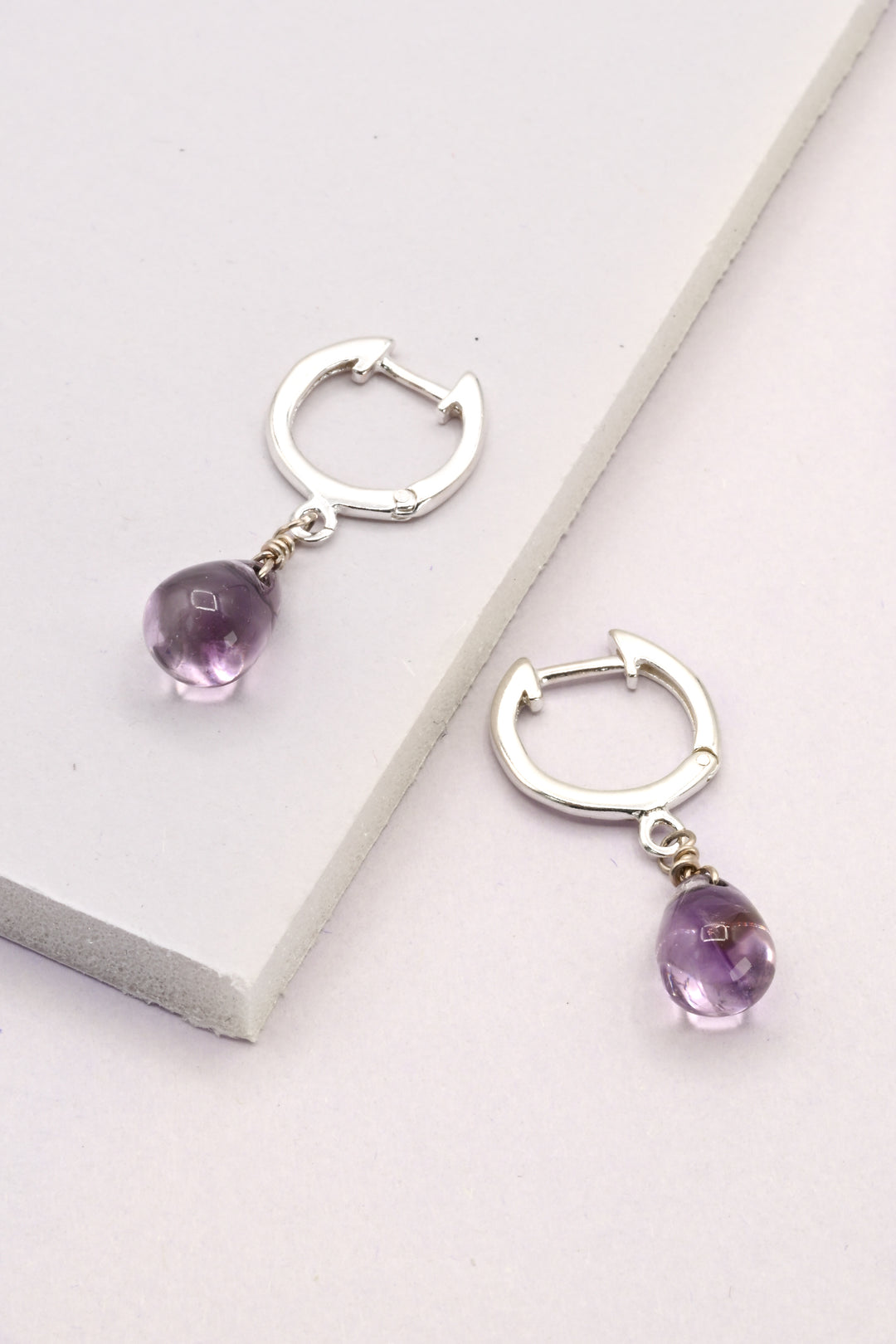 Silver hinged hoop earrings with purple amethyst teardrops.