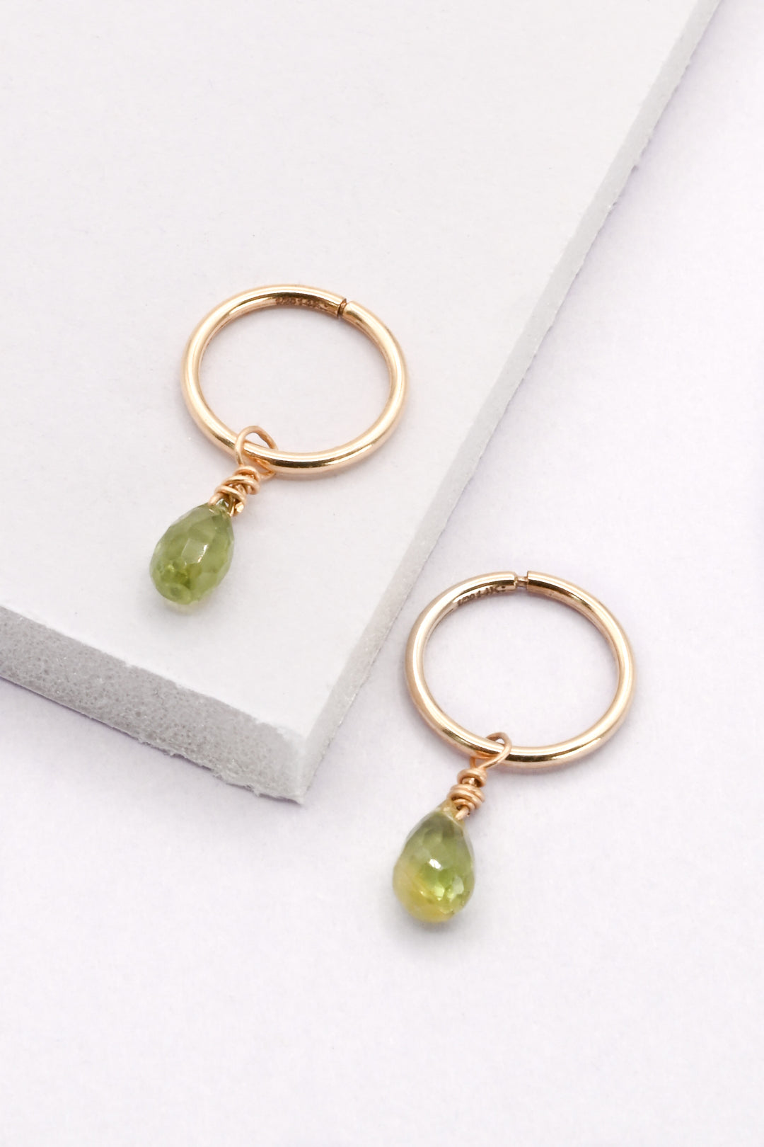Gold hoop earrings with faceted green sapphire teardrop charms on a white background.