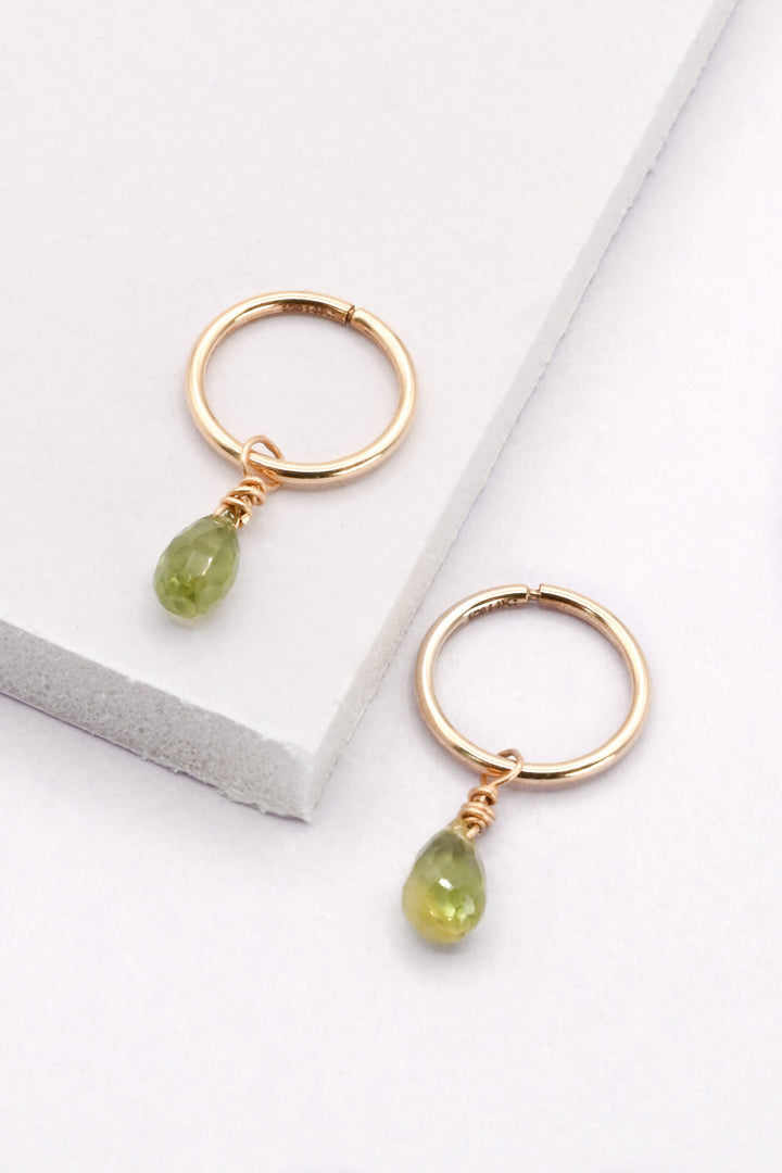 Gold hoop earrings with faceted green sapphire teardrop charms on a white background.