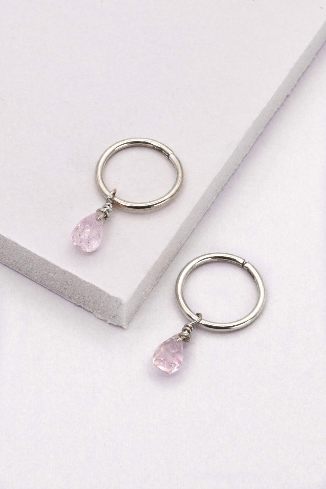 Small sterling silver seamless huggie hoop earrings with light pink sapphire charms.