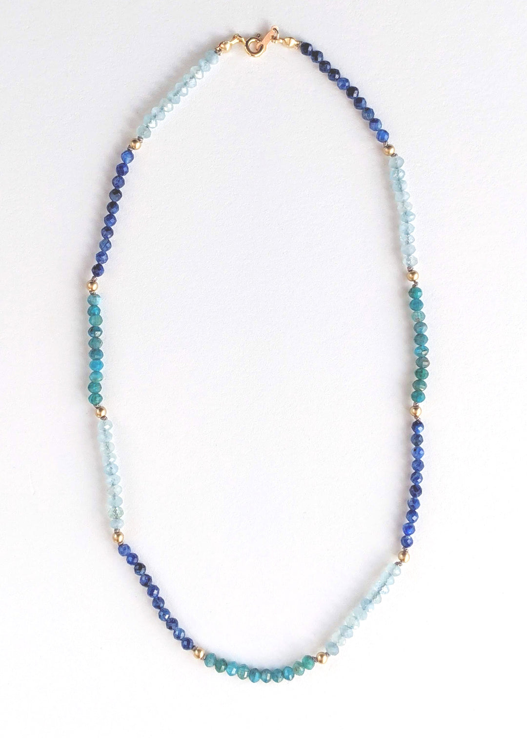 Portrait cropped image of a blue ombre beaded gemstone necklace with tiny beads of aquamarine, kyanite, and apatite. Gemstone beads strung on silk thread with gold accents beads and lobster clasp. Handcrafted jewelry by artist