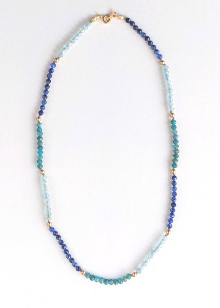 Portrait cropped image of a blue ombre beaded gemstone necklace with tiny beads of aquamarine, kyanite, and apatite. Gemstone beads strung on silk thread with gold accents beads and lobster clasp. Handcrafted jewelry by artist