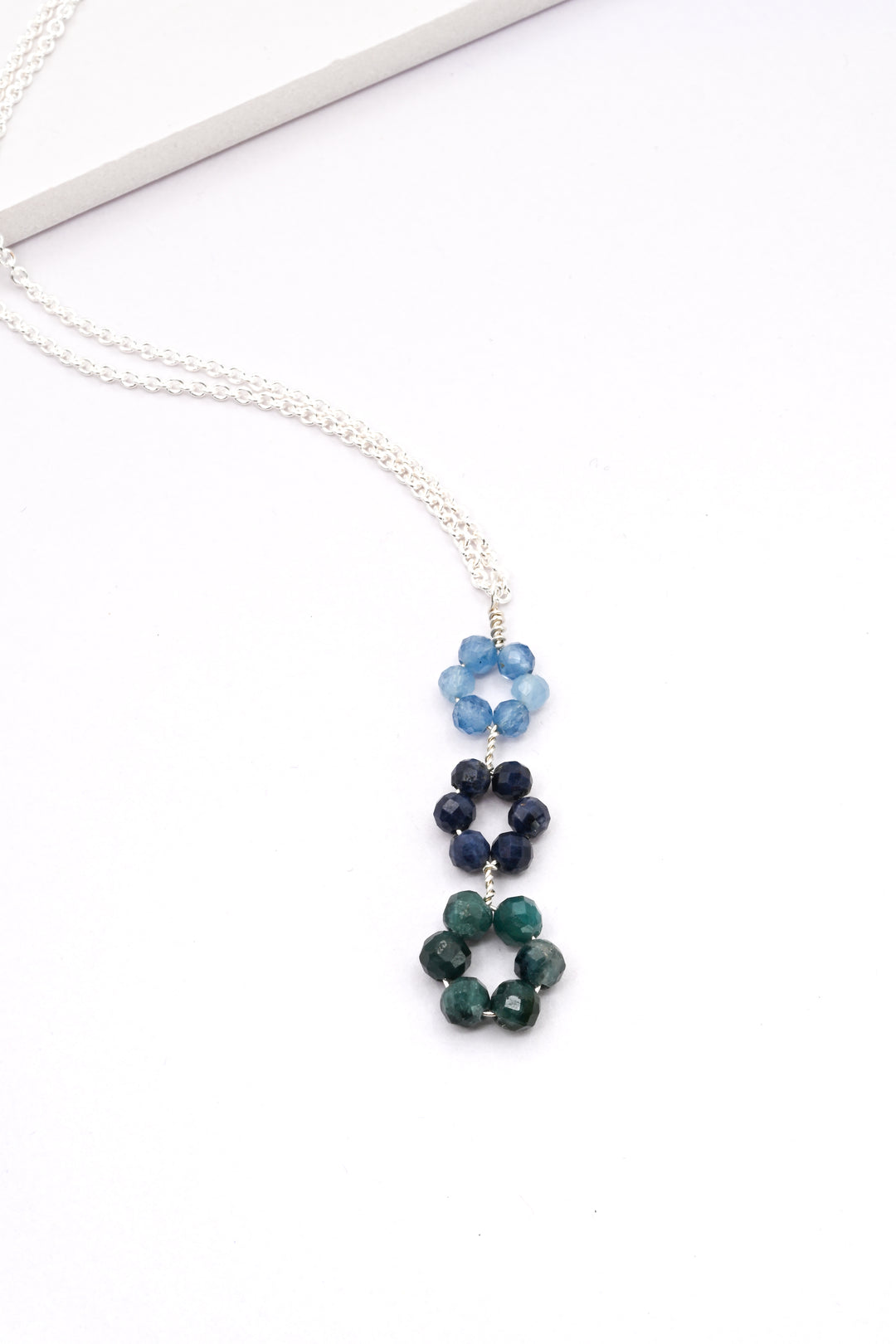Blue triple flower pendant with aquamarine, sapphire, and tourmaline daisies descending in a row, on a delicate sterling silver chain.