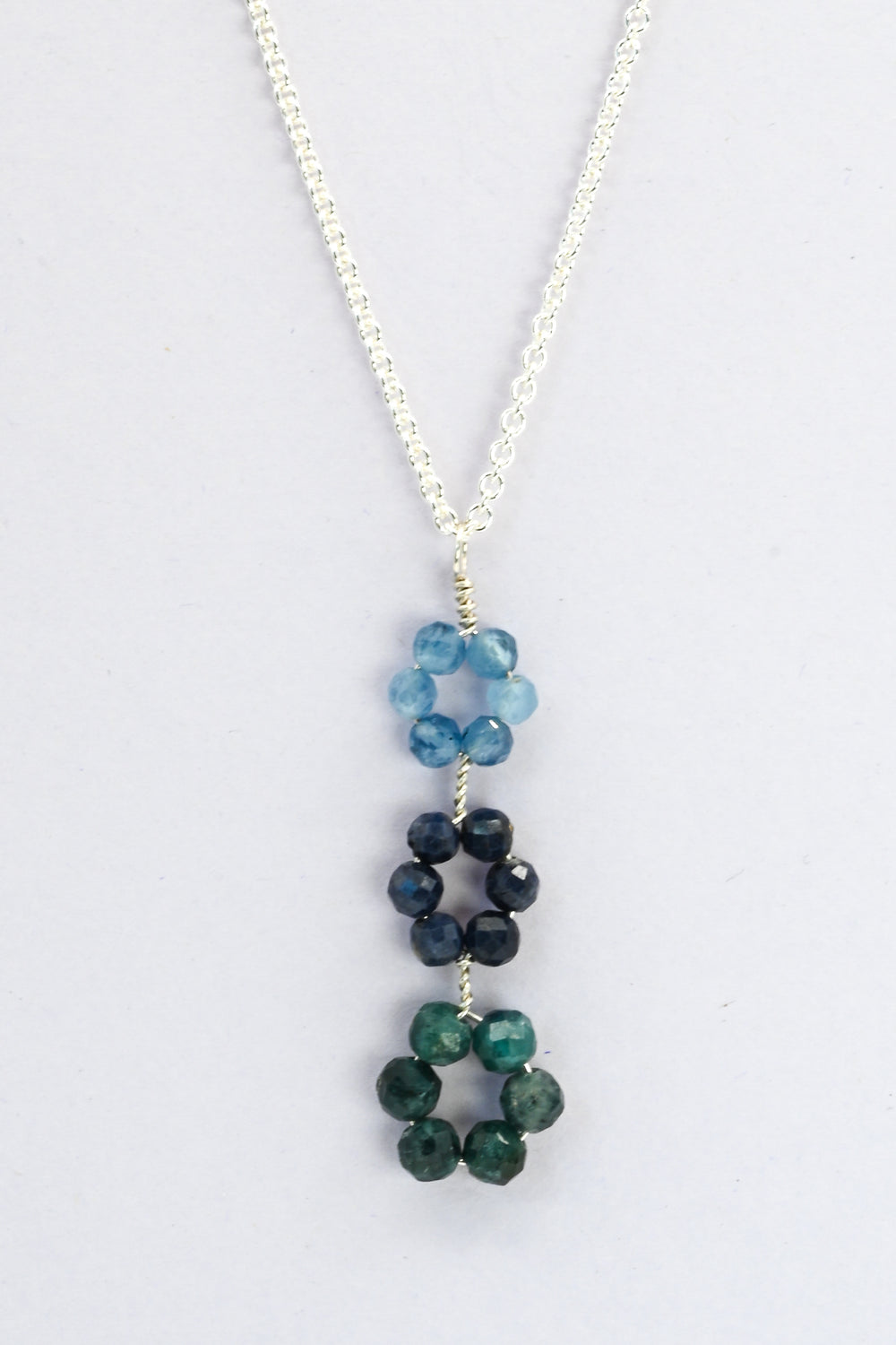 Blue triple flower pendant necklace with descending gemstone daisies in blue aquamarine, sapphire, and green tourmaline on a delicate sterling silver chain