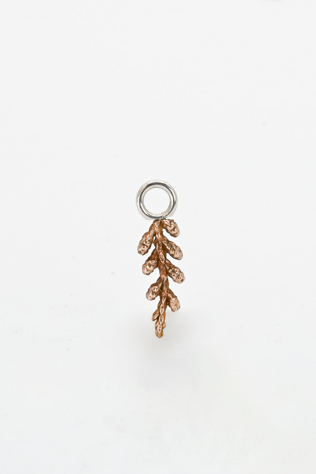 Tiny cast bronze charm of a juniper tree leaf with attached sterling silver ring to wear on a hoop earring, charm bracelet, or charm necklace.