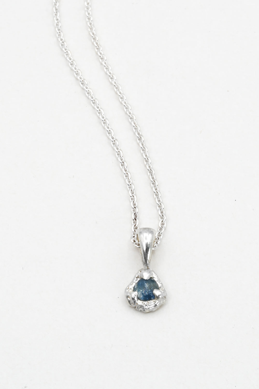 Silver necklace with a light blue sapphire pendant on a white background