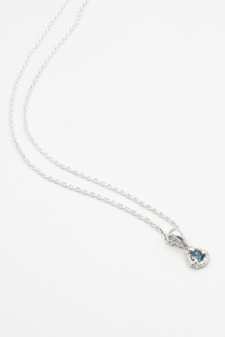 Silver necklace with a light blue sapphire pendant on a white background