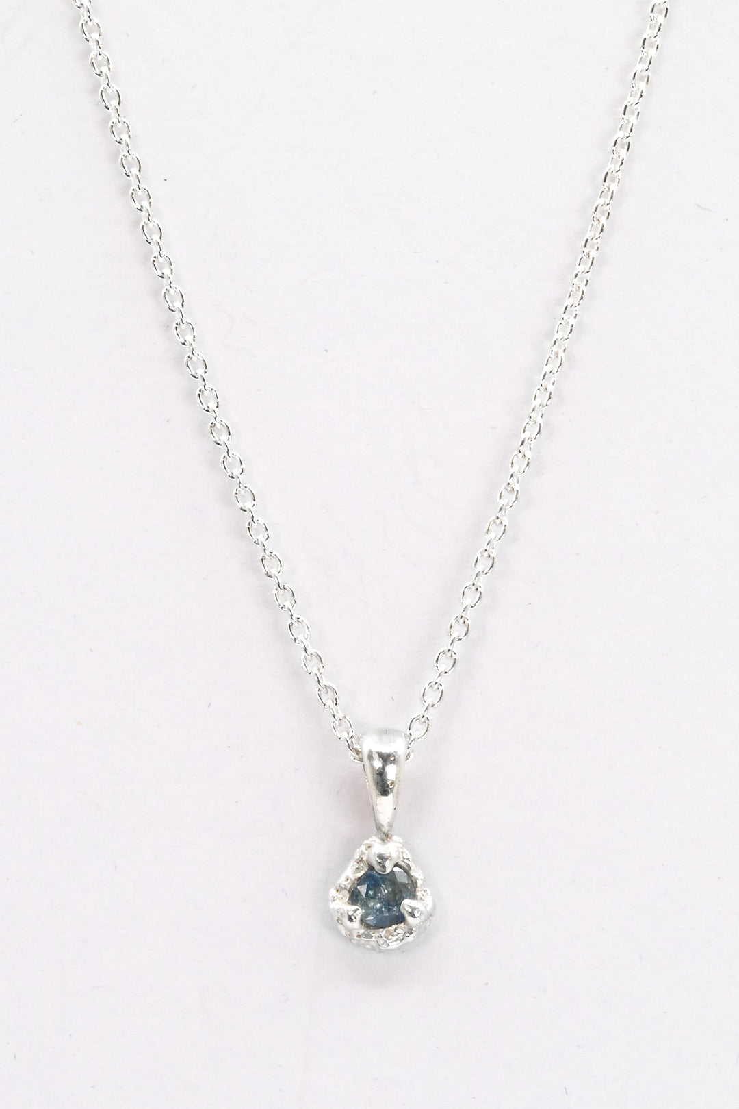 Silver necklace with a pendant featuring a light blue sapphire on a white background
