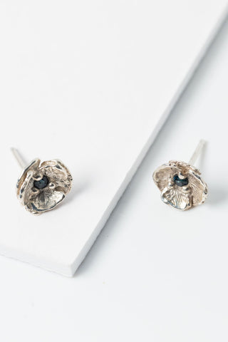 Small dainty flower earrings with Montana sapphire centers and layered realistic petals on sterling silver posts on a white background, seen slightly from above. 