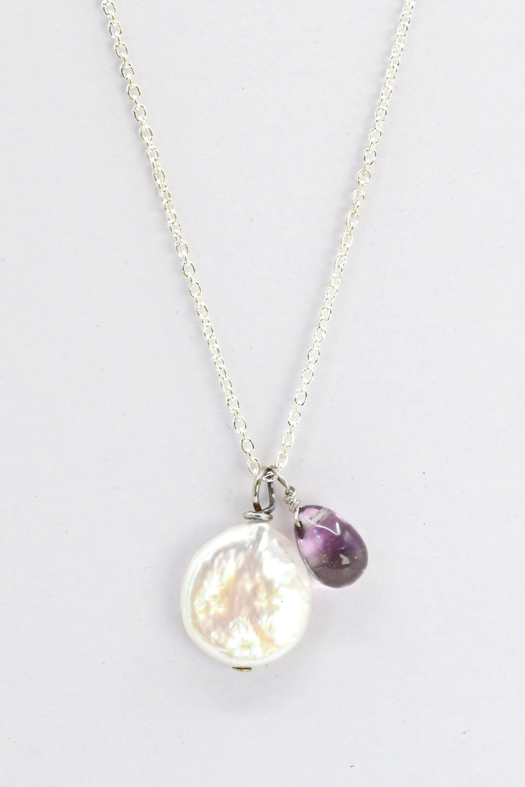A sterling silver charm  necklace with a freshwater coin pearl and small teardrop amethyst on a delicate silver chain. 