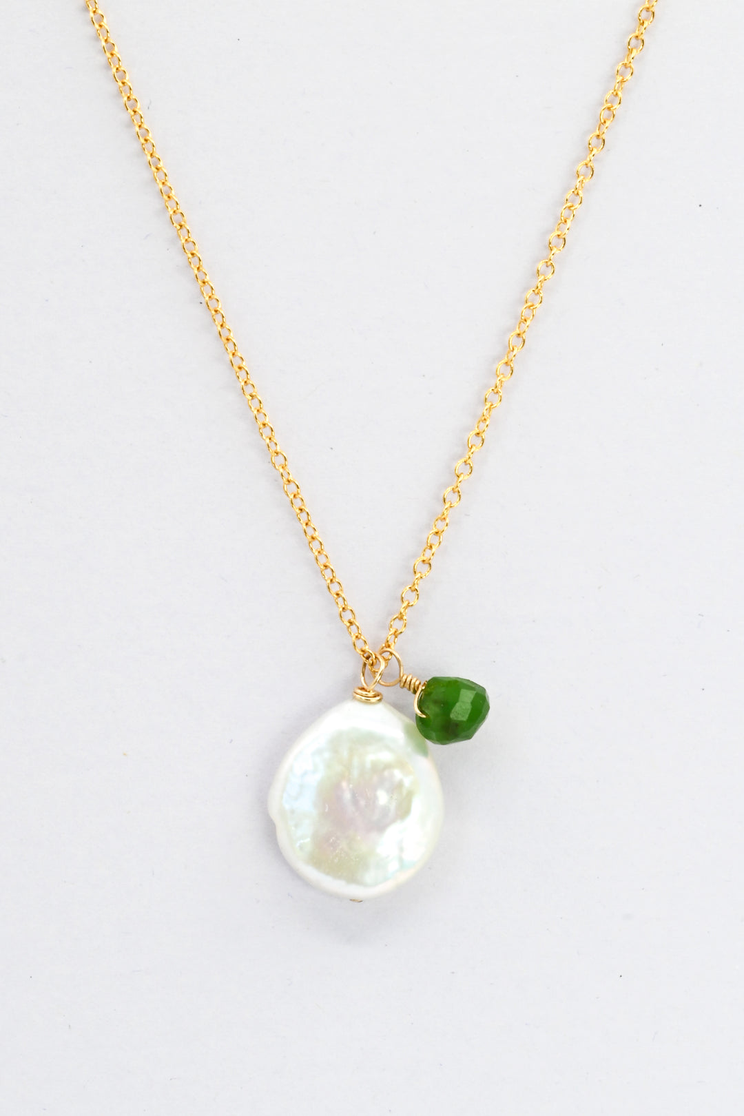 A delicate gold charm necklace with a white freshwater coin pearl and small green jade teardrop.
