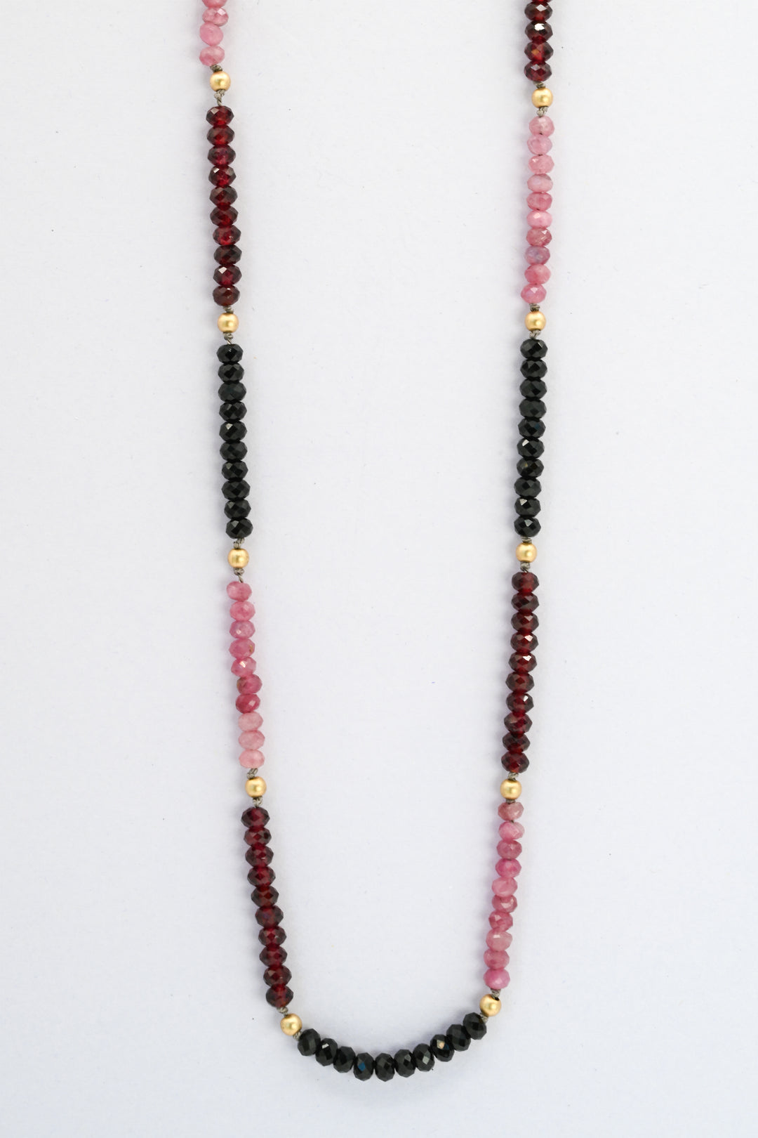 Beaded gemstone necklace with color blocked sections in pink tourmaline, red garnet, and black spinel, divided by round gold beads
