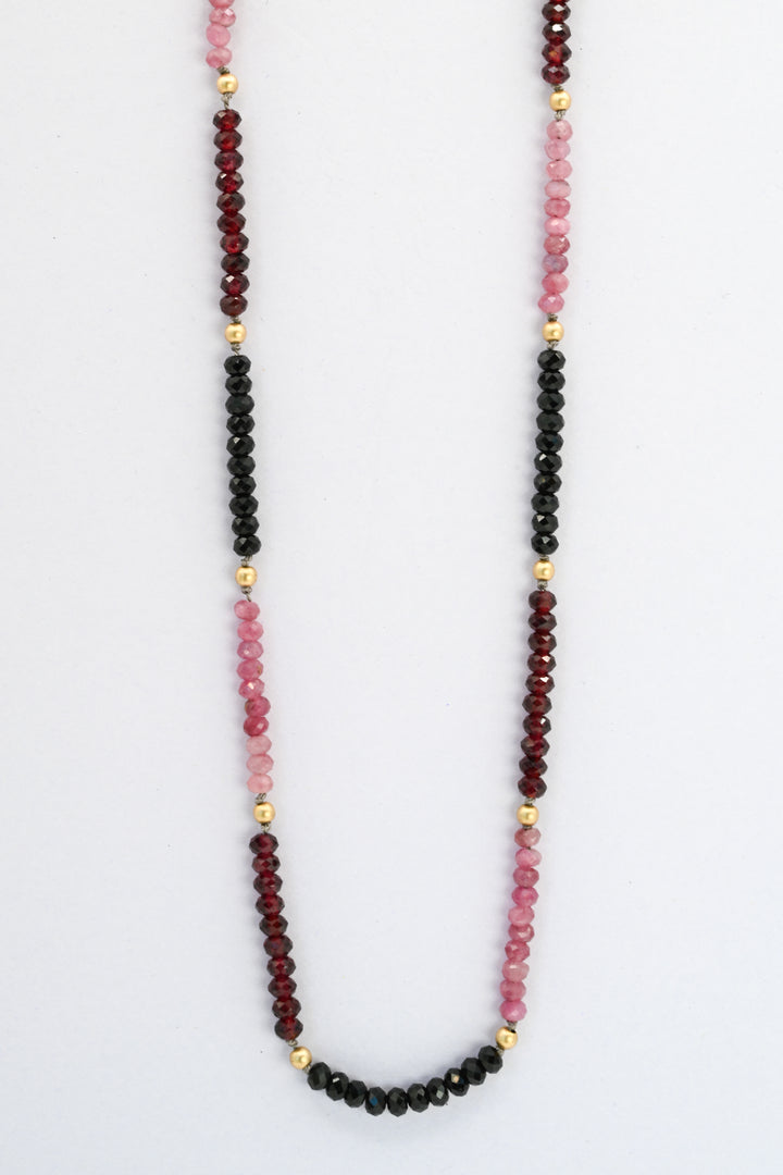 Beaded gemstone necklace with color blocked sections in pink tourmaline, red garnet, and black spinel, divided by round gold beads