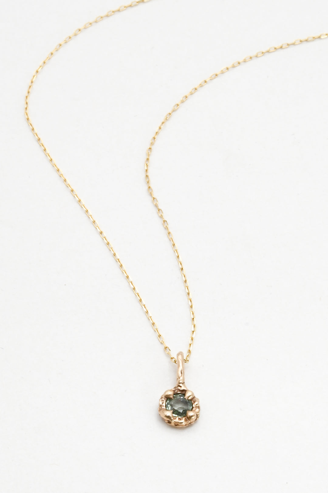Gold necklace with a green sapphire pendant on a white background