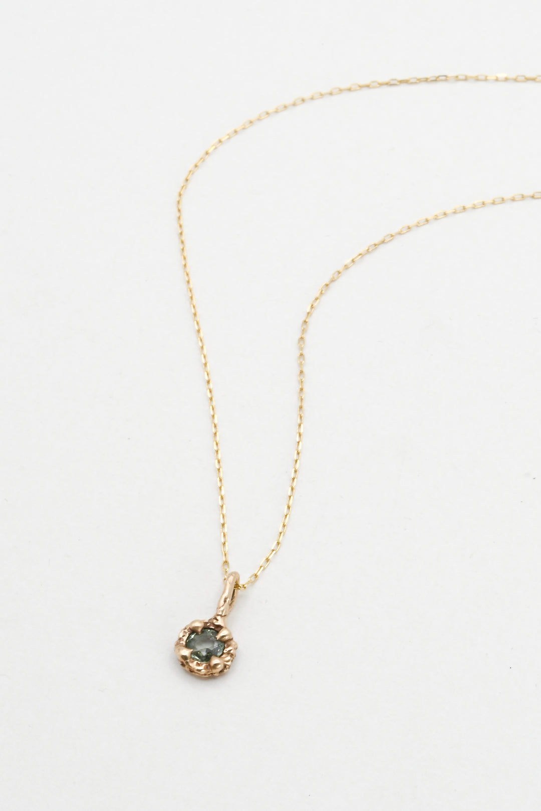 Gold necklace with a green sapphire pendant on a white background 