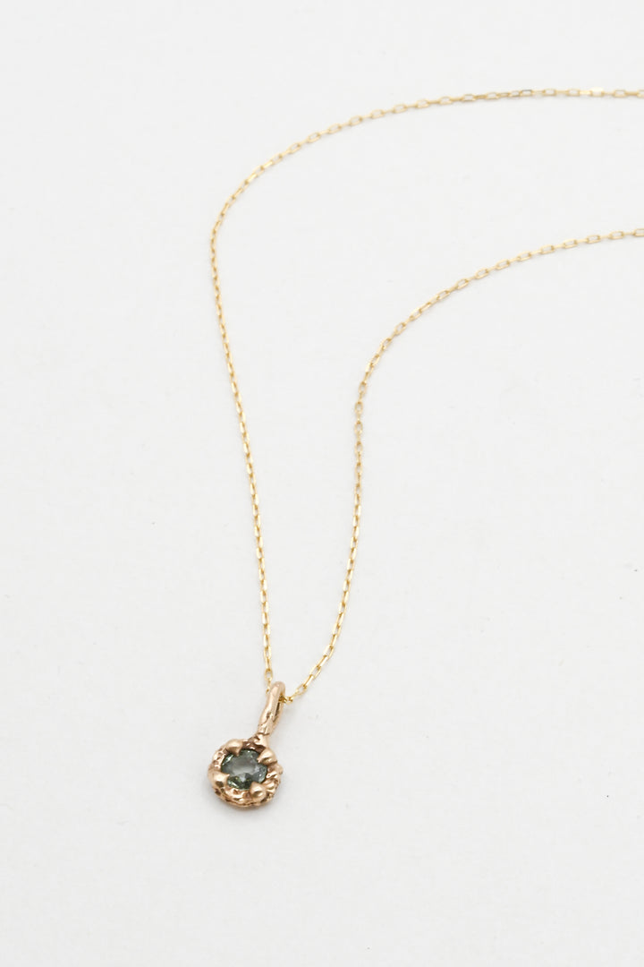 Gold necklace with a green sapphire pendant on a white background 