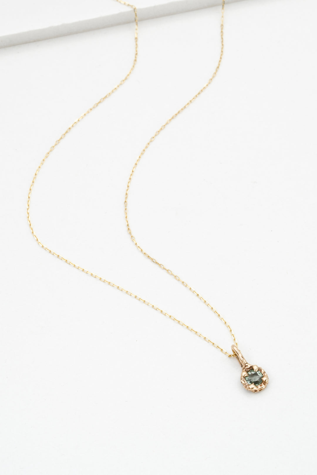 Gold necklace with a green sapphire pendant on a white background