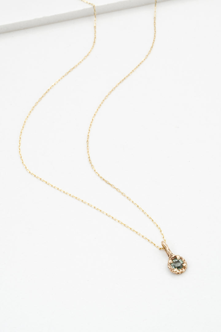 Gold necklace with a green sapphire pendant on a white background