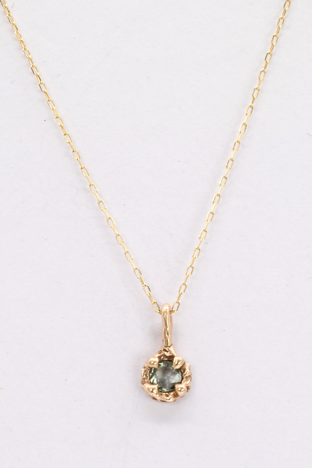 Gold necklace with a pendant featuring a green gemstone on a white background
