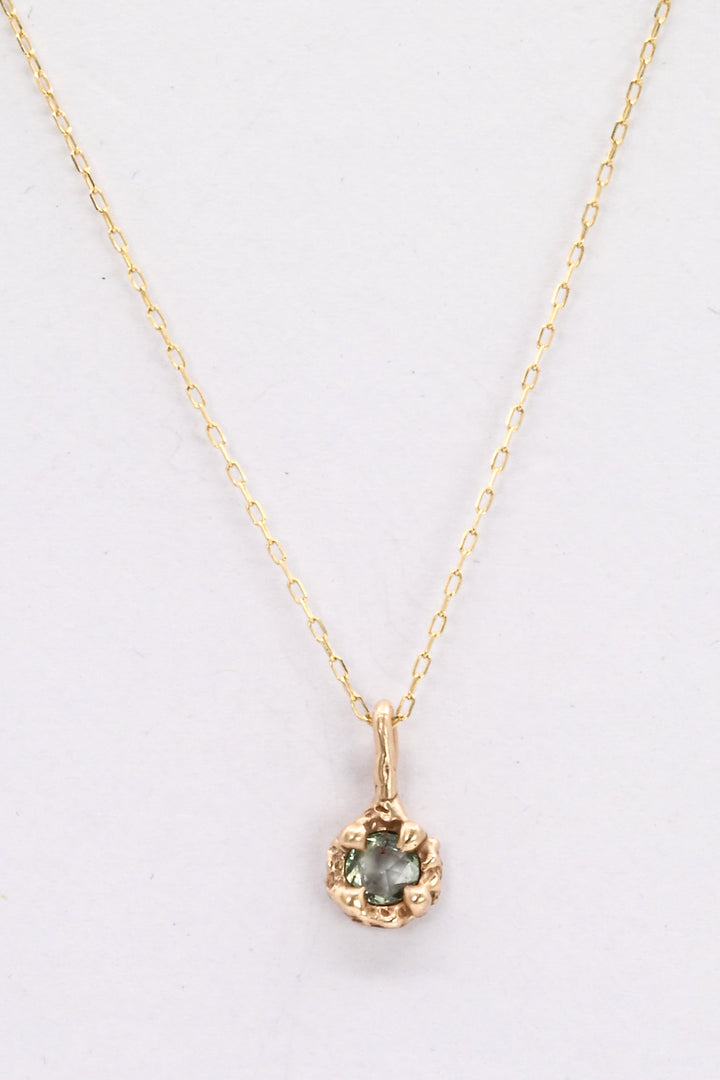 Gold necklace with a pendant featuring a green gemstone on a white background
