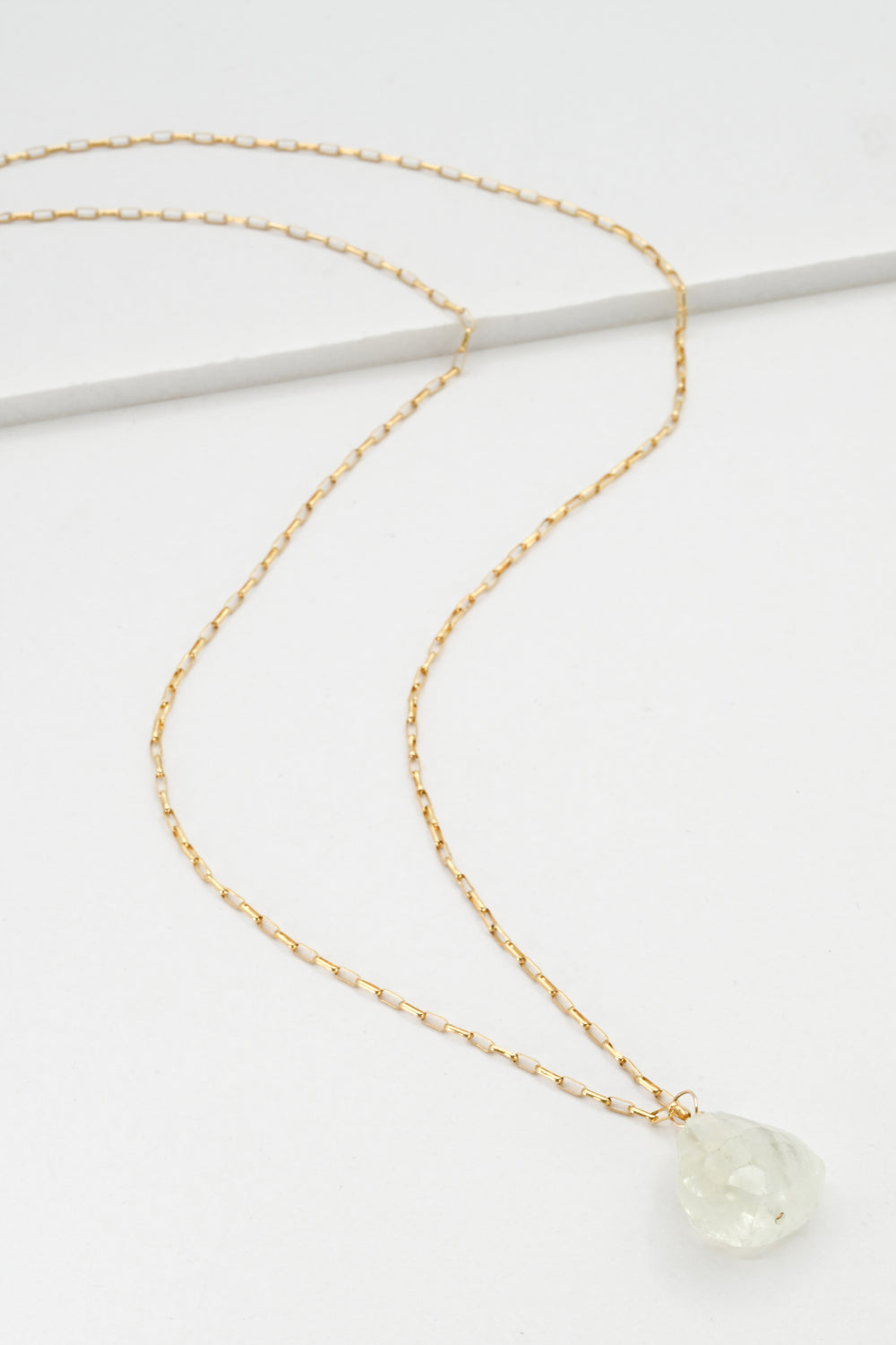 Gold necklace with a green aquamarine pendant on a white background