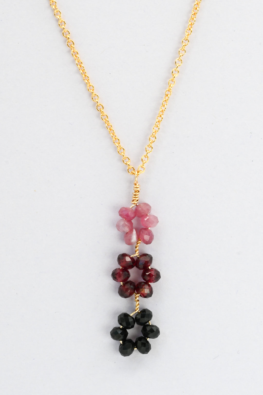 Triple flower pendant necklace in descending daisy pattern of pink tourmaline, red garnet, and black spinel on a delicate gold chain