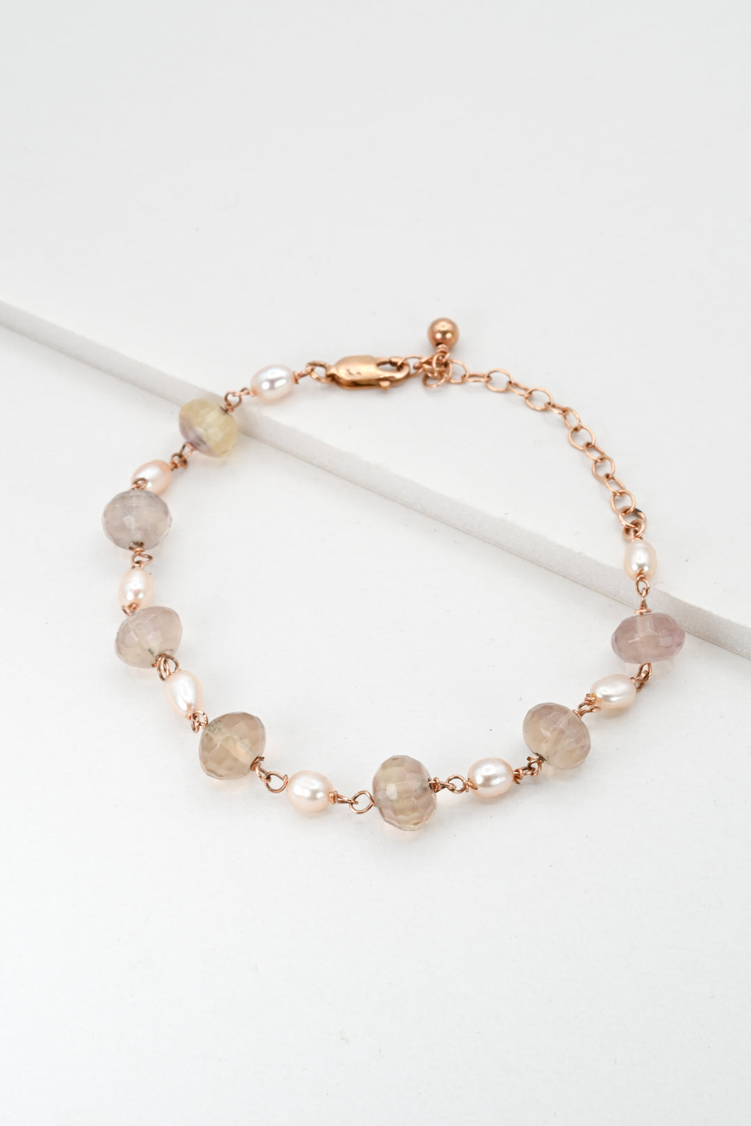 Rose gold link bracelet with purple fluorite and pink freshwater pearl beads and an extender chain on a white background.