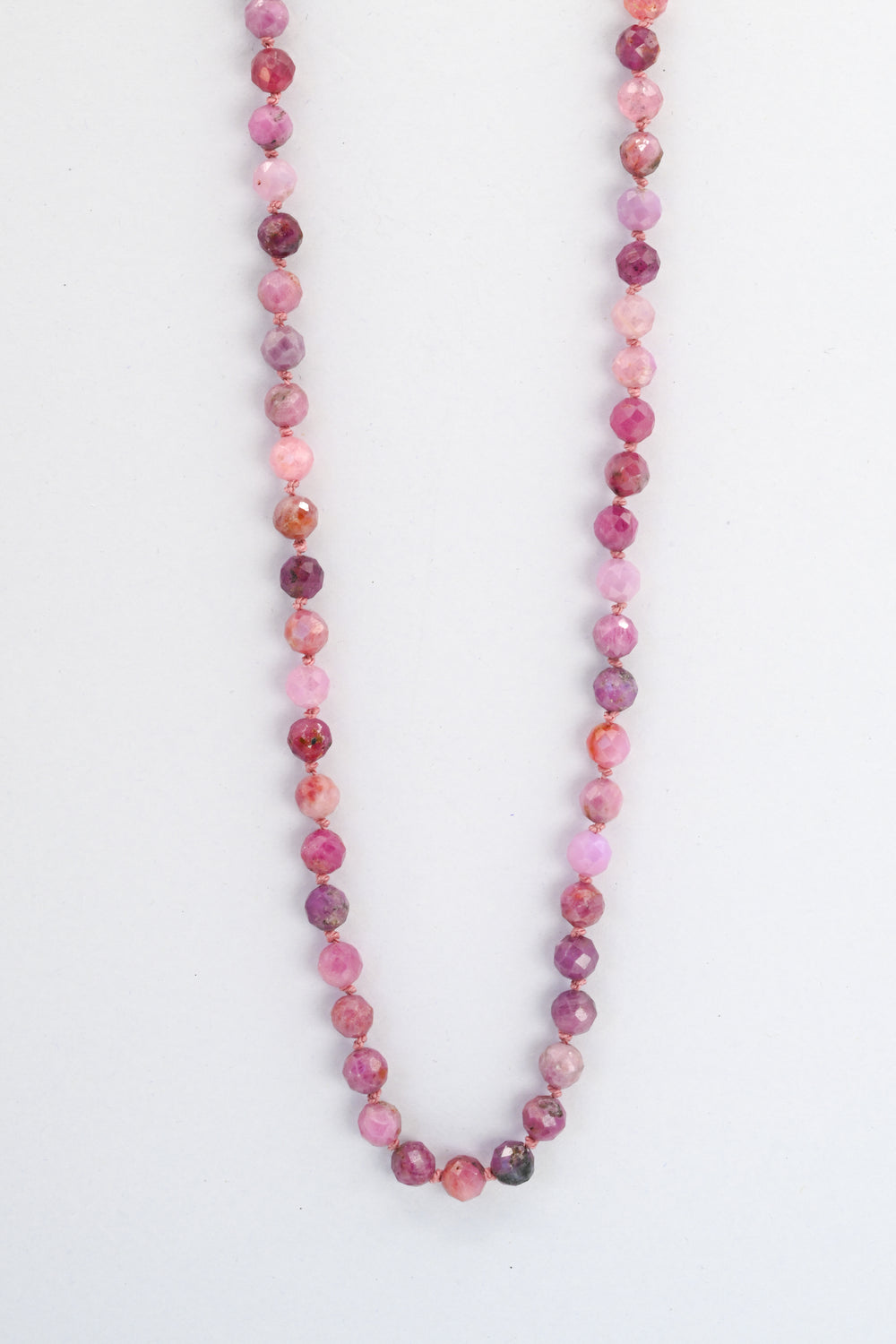 Natural pink ruby beaded necklace hanging on a white background