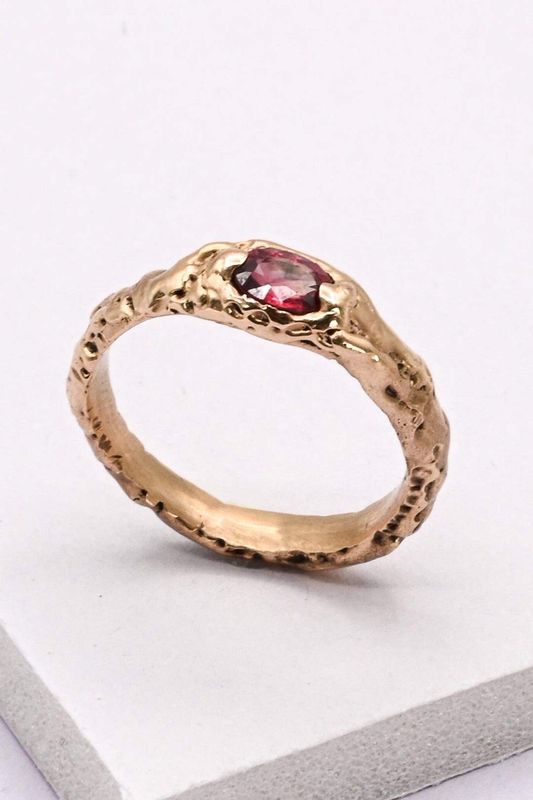 Textured gold ring with a scarlet red oval sapphire focal gemstone on a white background