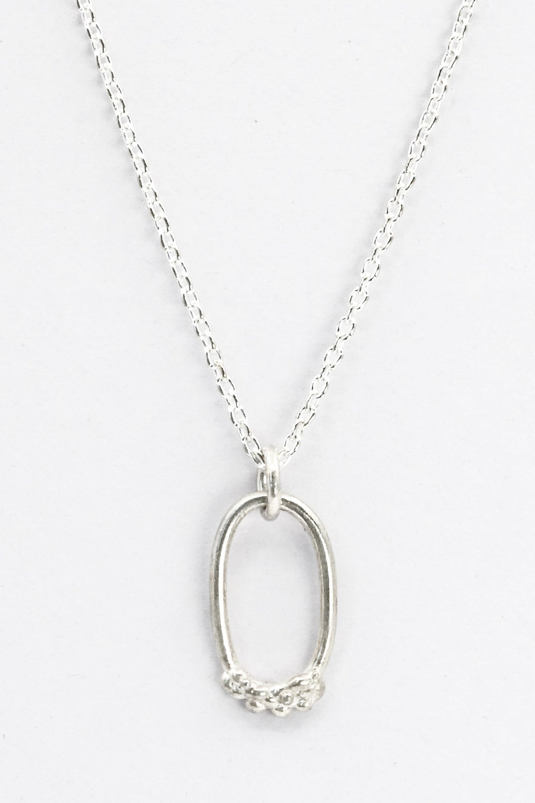 Cast silver oval pendant necklace with organic bubble texture on its bottom edge