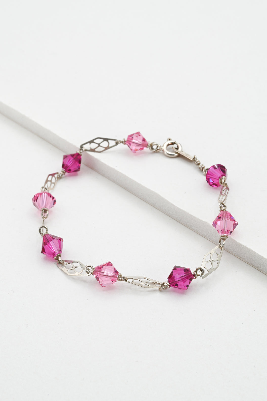 Silver link bracelet with light and dark pink crystals on a white background