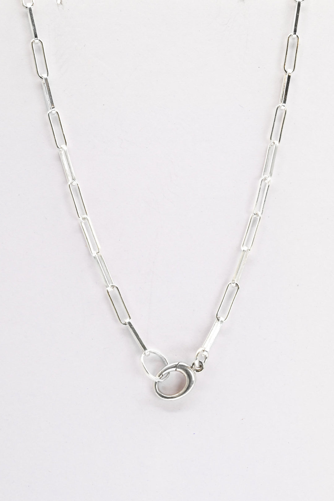 Sterling silver paperclip chain with charm holder clasp on a white background