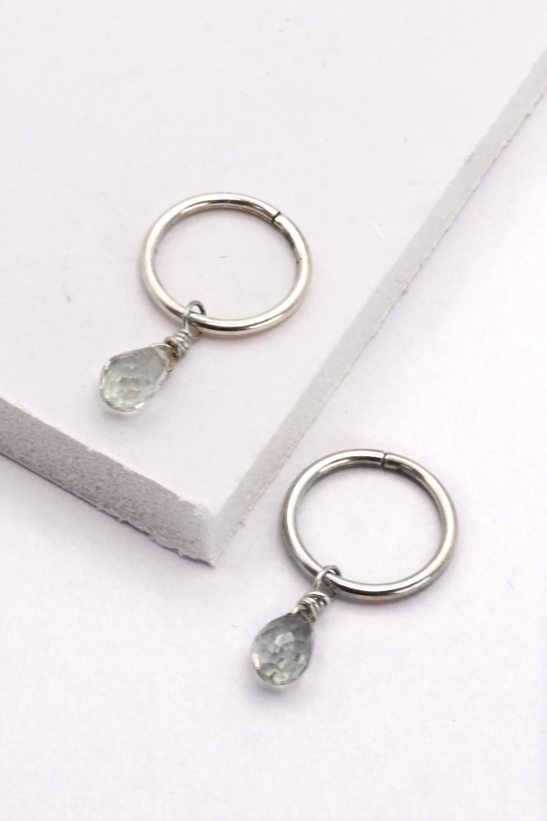 Small silver huggie hoop earrings with silver sapphire teardrop charms.