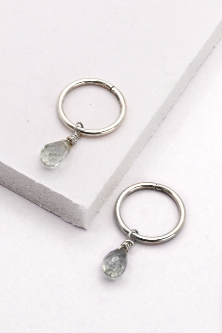 Small silver huggie hoop earrings with silver sapphire teardrop charms.