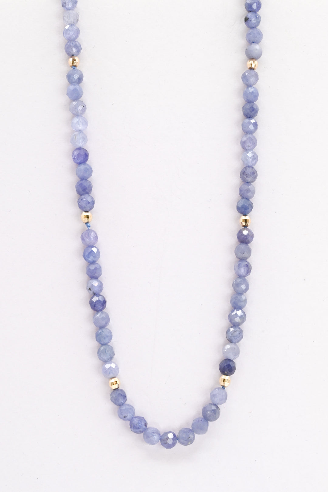 Purple tanzanite and 14k yellow gold beaded necklace against a white background 