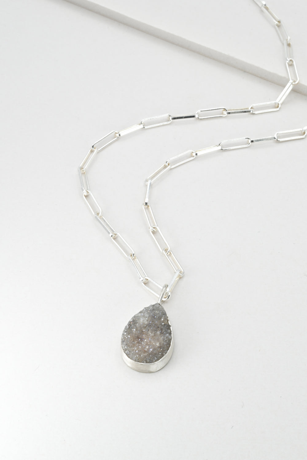 Silver necklace with a purple teardrop pendant on a white background