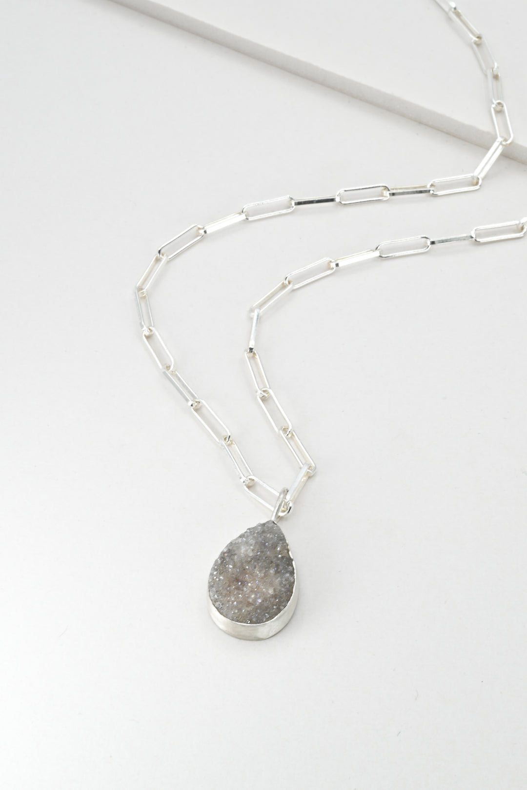 Silver necklace with a purple teardrop pendant on a white background