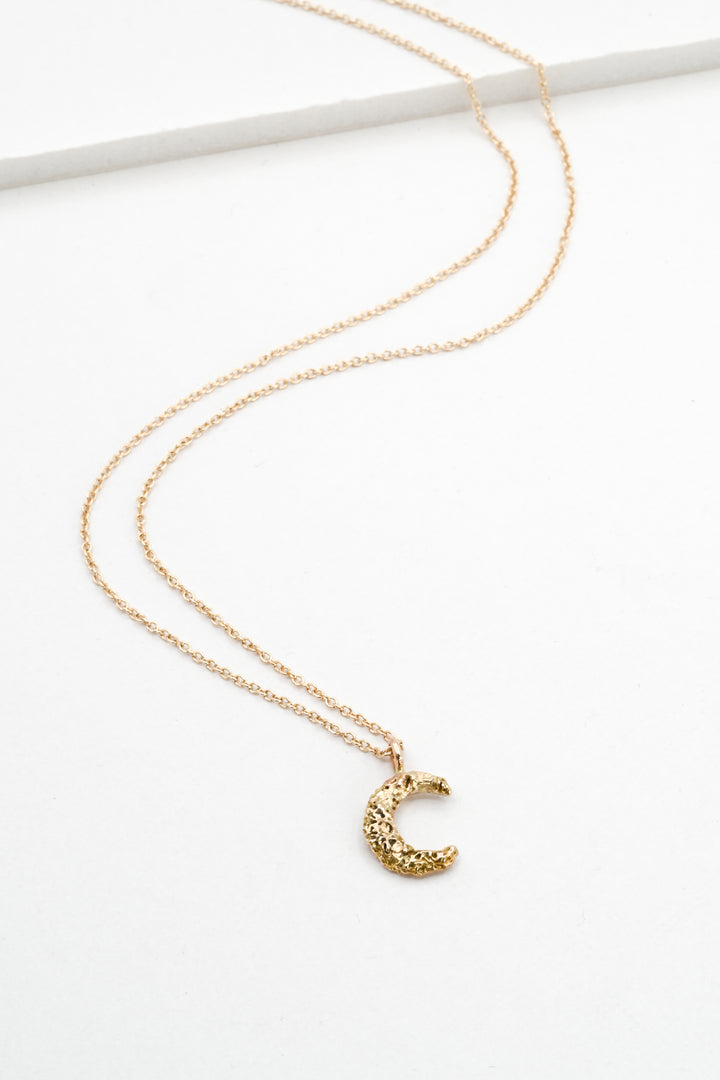 Small textured gold moon pendant necklace on a white background