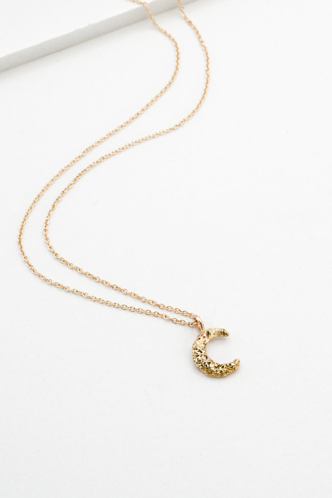 Small textured gold moon pendant necklace on a white background