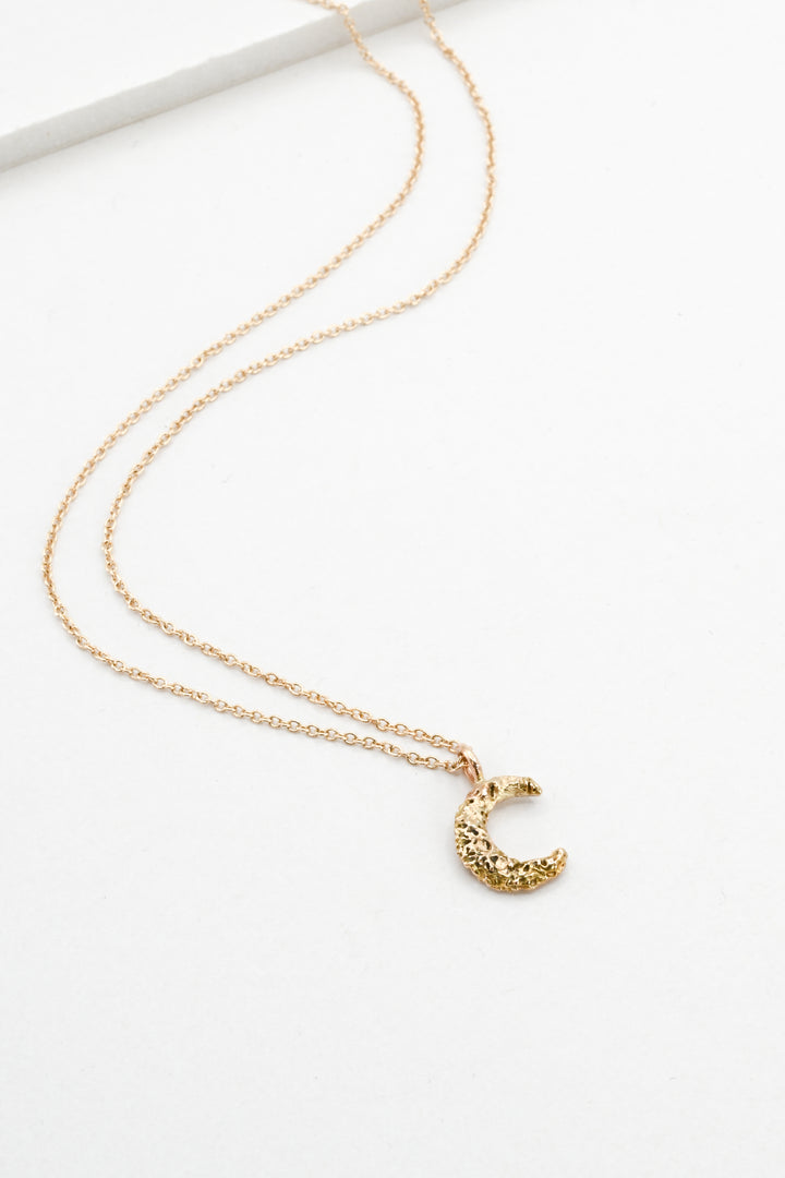 Small textured gold moon pendant necklace on a white background