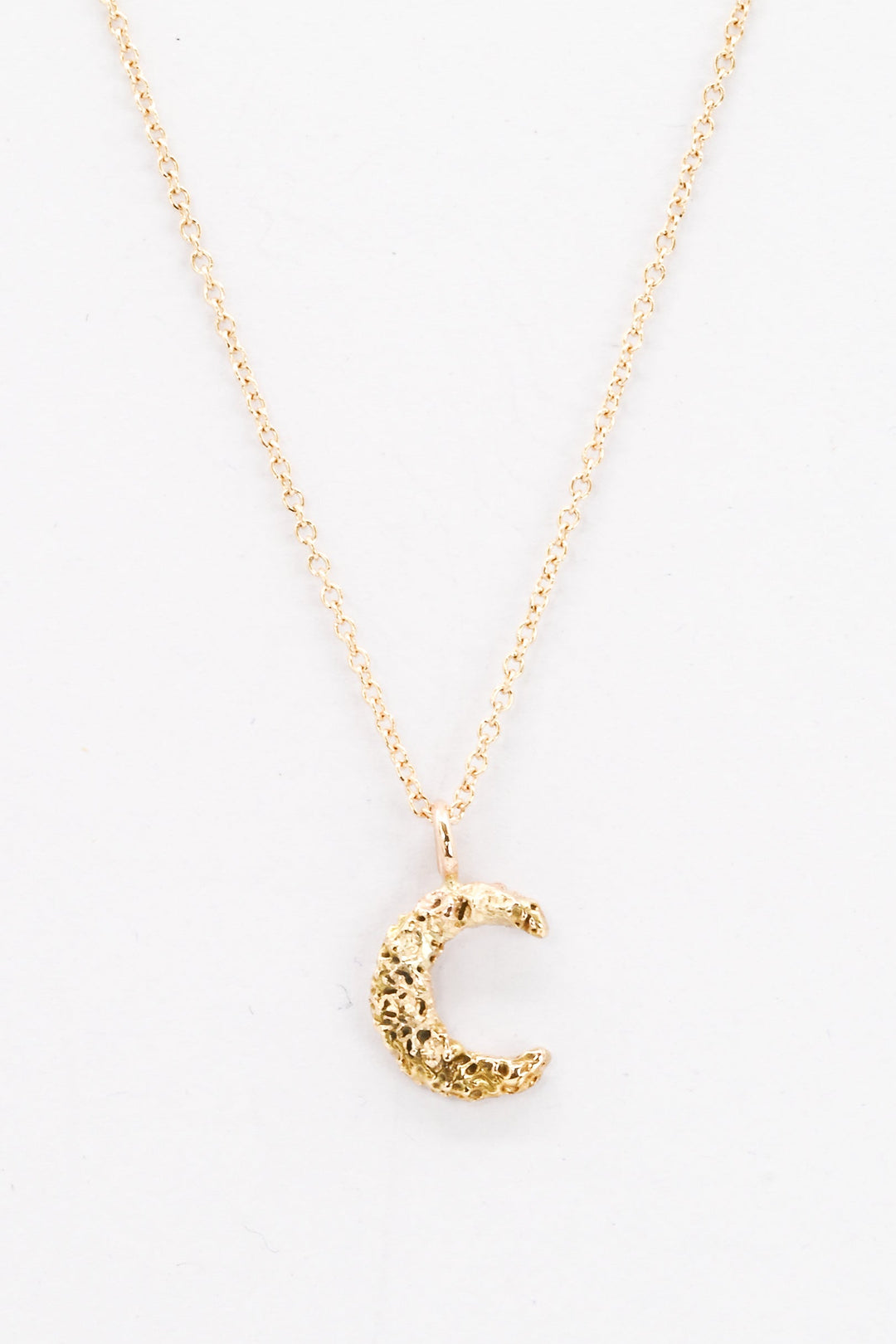Small textured gold moon pendant necklace on a white background