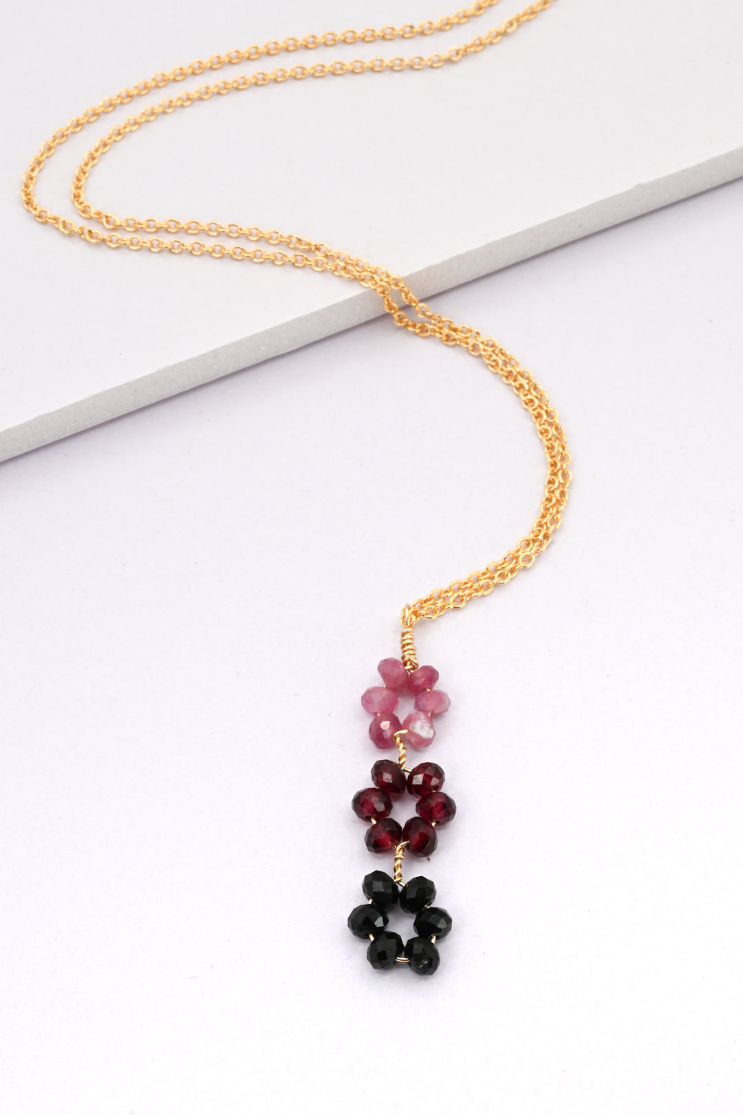 Delicate gold necklace with a pendant of 3 flowers in pink tourmaline, red garnet, and black spinel, by J'Adorn Designs.