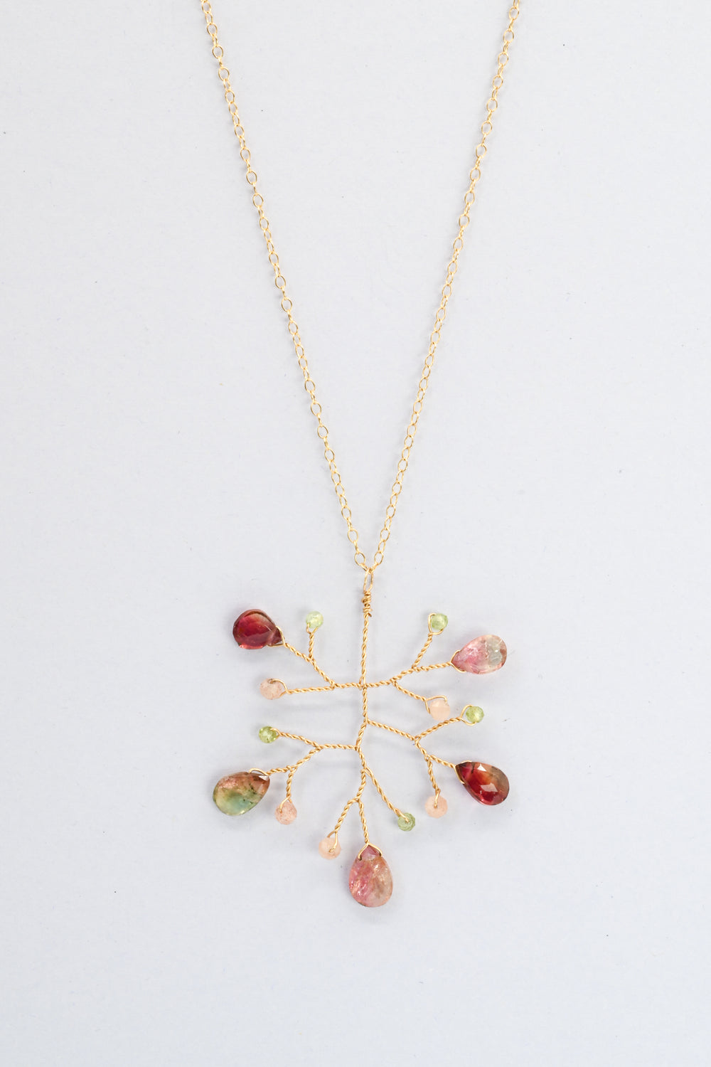 Delicate vine pendant necklace with watermelon tourmaline teardrops and accent beads in green peridot and peach moonstone, on a delicate gold chain against a white background