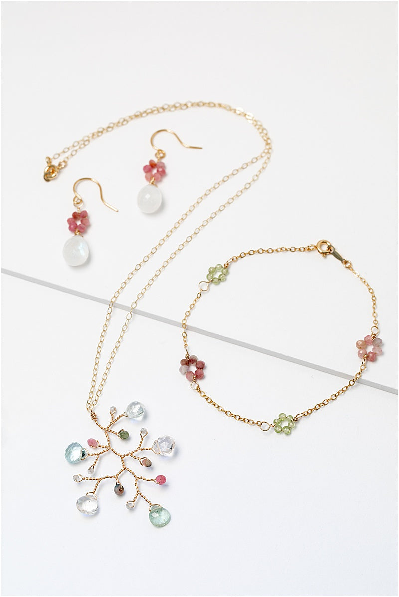 A matching gold jewelry collection with colorful gemstone flowers. Jewelry set features a necklace, a bracelet, and a pair of earrings. For sale: one handcrafted gold pendant featuring a wire-wrapped branch with aquamarine teardrops and tourmaline beads in a rainbow of colors. A lightweight, hypoallergenic gemstone necklace on a fine 14k gold filled chain. Artisan jewelry made by Alison Jefferies for J'Adorn Designs.