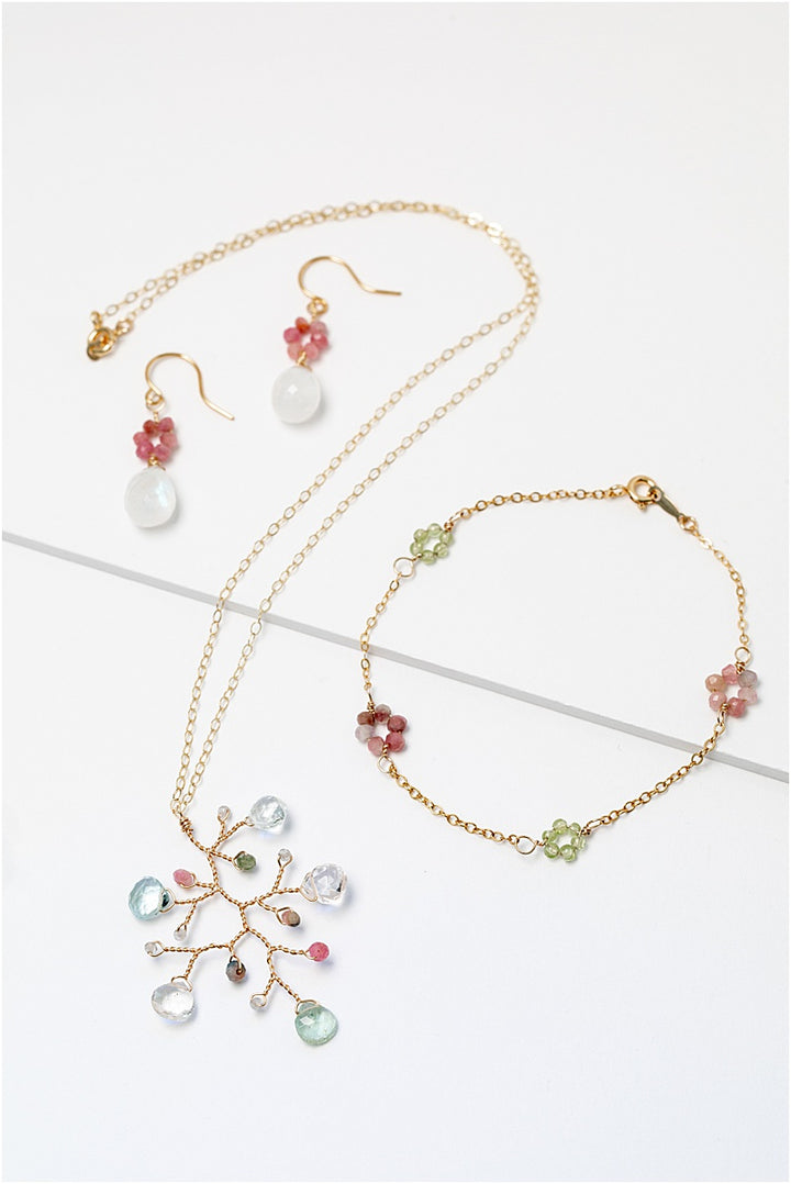 A matching gold jewelry collection with colorful gemstone flowers. Jewelry set features a necklace, a bracelet, and a pair of earrings. For sale: one handcrafted gold pendant featuring a wire-wrapped branch with aquamarine teardrops and tourmaline beads in a rainbow of colors. A lightweight, hypoallergenic gemstone necklace on a fine 14k gold filled chain. Artisan jewelry made by Alison Jefferies for J'Adorn Designs.