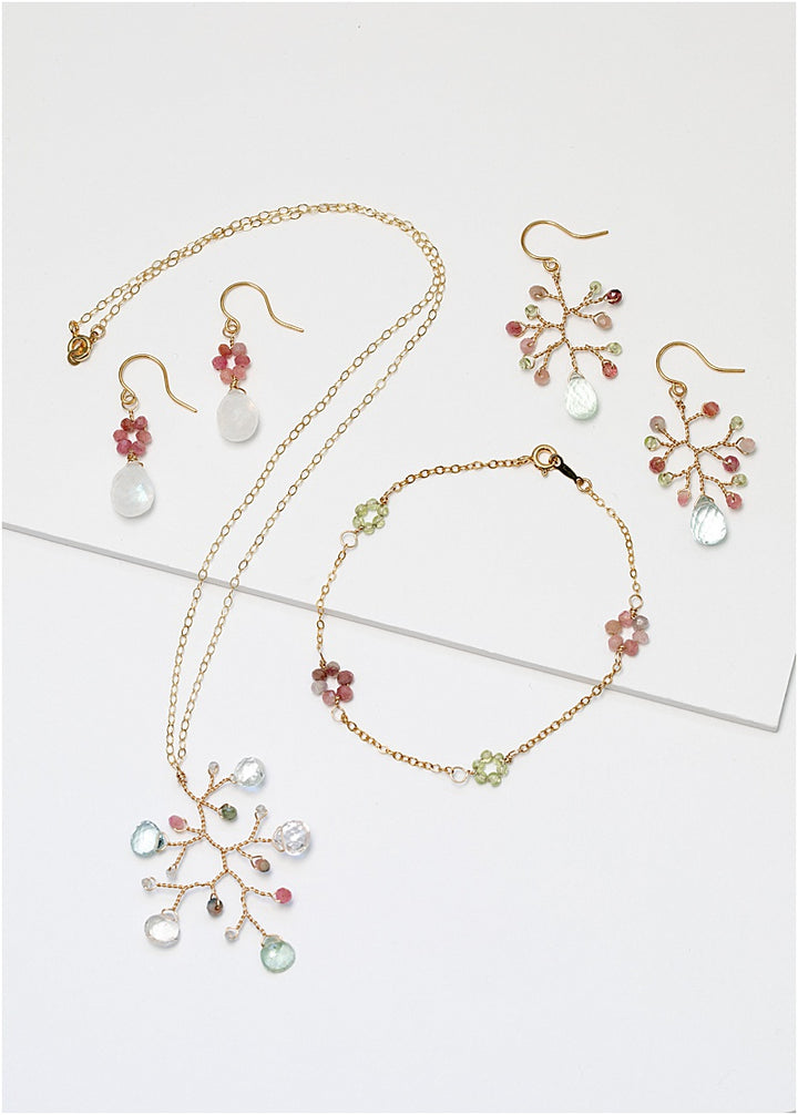 A matching gold jewelry collection with colorful gemstone flowers. Jewelry set features a necklace, a bracelet, and two pairs of earrings. For sale: one handcrafted gold pendant featuring a wire-wrapped branch with aquamarine teardrops and tourmaline beads in a rainbow of colors. A lightweight, hypoallergenic gemstone necklace on a fine 14k gold filled chain. Artisan jewelry made by Alison Jefferies for J'Adorn Designs.