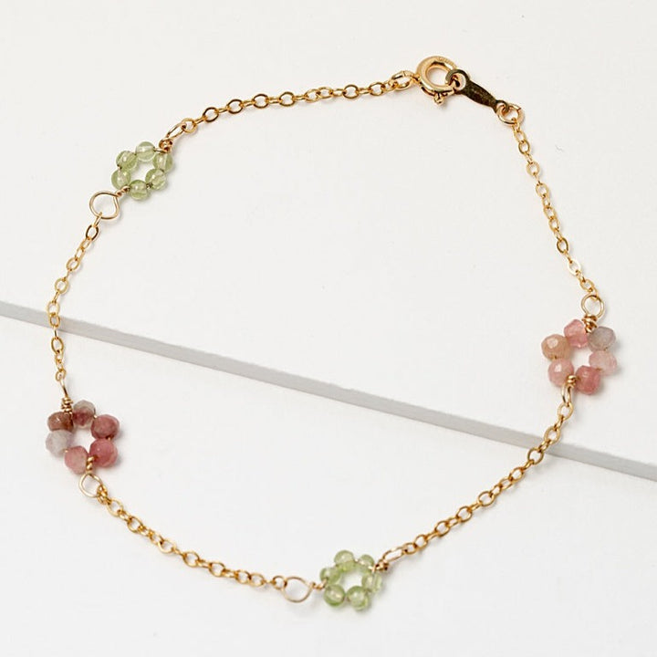 Gold daisy chain bracelet with green peridot and pink tourmaline gemstone "flowers" on a delicate golden chain. Handcrafted jewelry and custom bridal accessories by J'Adorn Designs artist Alison Jefferies.
