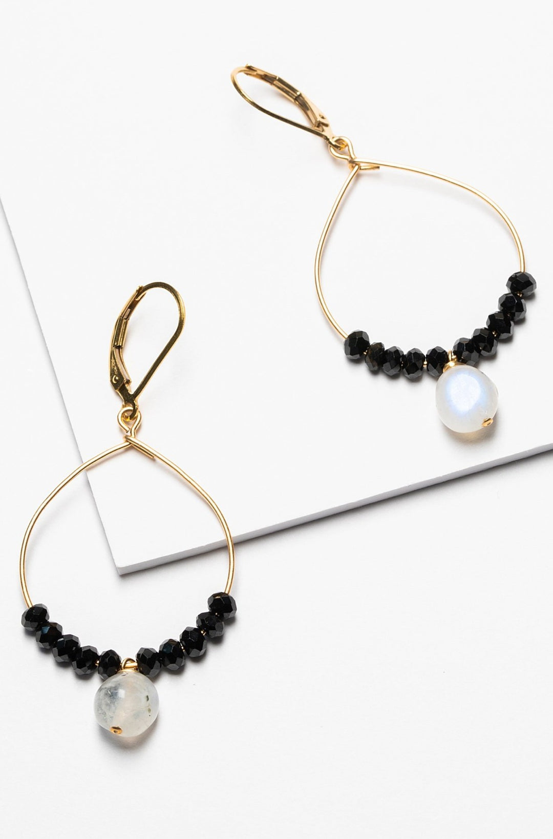 Black and gold handcrafted hoop earrings for sale. A pair of delicate gold hoops with black spinel and moonstone bead accents for luxury fashion or a jewelry gift idea. Artisan jewelry and luxury bridal accessories handmade in Maryland by Alison Jefferies of J'Adorn Designs.