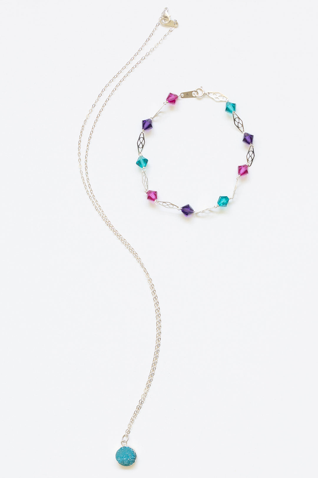 Delicate silver link bracelet for stacking or wedding jewelry. Jewel tone Swarovski crystals in pink, purple, and turquoise with silver filigree links, styled with a blue druzy pendant necklace with silver bezel setting. Mermaid colors silver bracelet. Artisan jewelry and luxury bridal accessories handmade in Maryland by Alison Jefferies of J'Adorn Designs.